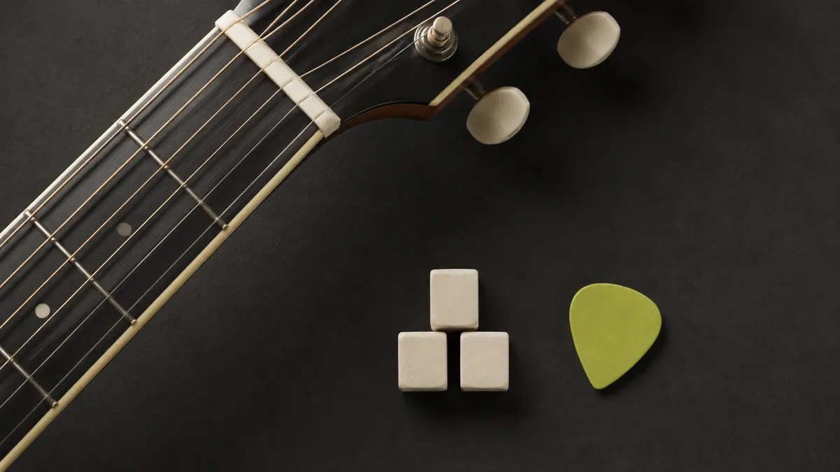 Three ivory blocks and a lime pick resting beside an acoustic guitar neck.